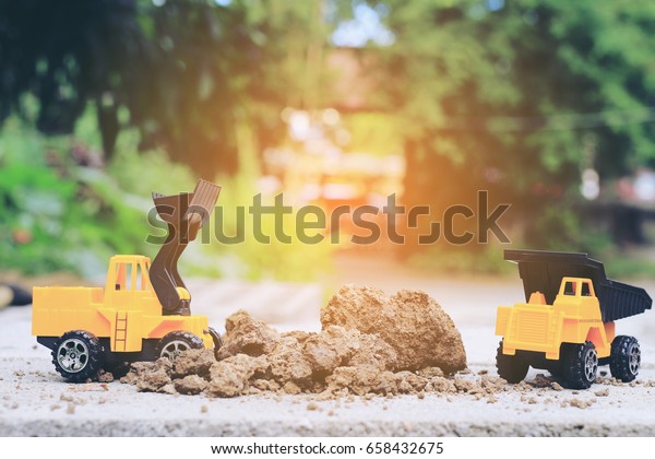 Truck toy car with sand and\
soil on the concrete floor with blur boken green environment \
construction equipment at work ,construction concept, selective\
focus.