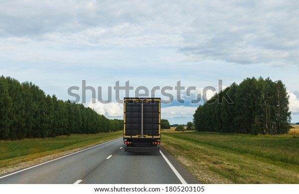A truck with a trailer is moving\
along the summer highway between cities. blurry\
focus