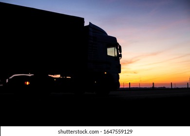 A truck with a trailer rides on the motorway at night against the backdrop of an orange sunny sunset. The concept of the regime of work and rest of truckers, copy space, tachograph