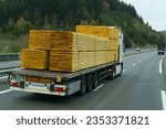 A truck transports lumber - boards on a motorway on a semi-trailer. In the background forest and mountains. Logistic concept.