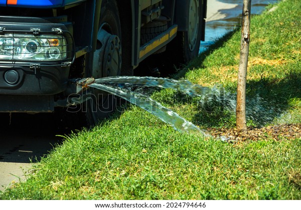 A truck for watering the\
lawn pours water on the lawn with water jets. City lawn care\
services.\
