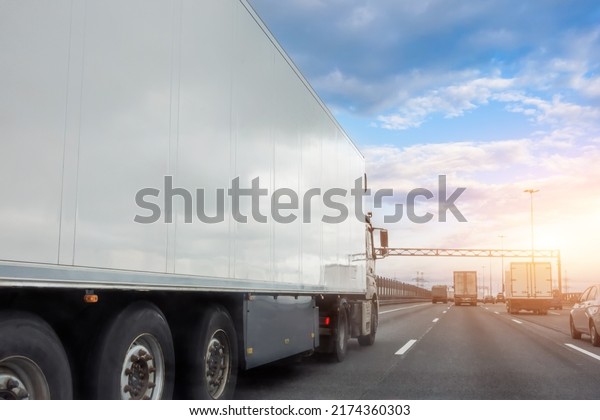 Truck with a white trailer drives\
along the highway in heavy traffic in the evening at\
sunset