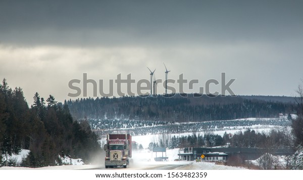 Truck in a winter landscape on a road with\
wind turbines in the\
background