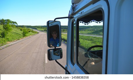 Trucker In Sunglasses Reflecting In Side Mirror Of Moving Car. Man Driving Lorry Riding To Destination Through Countryside Road. Cargo Transportation Concept. Beautiful Background. Slow Mo Close Up