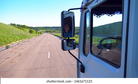 Trucker In Sunglasses Reflecting In Side Mirror Of Moving Car. Man Driving Lorry Riding To Destination Through Countryside Road. Cargo Transportation Concept. Beautiful Background. Slow Mo Close Up