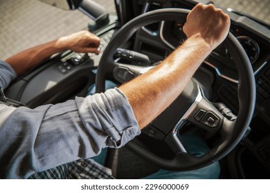 Truckers Hand on a Semi Truck Steering Wheel Close Up Photo. Caucasian Professional Driver Theme. Transportation Industry.