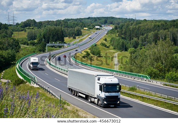 Trucks\
and cars driving on a highway through a forested hill and a bridge\
across the valley. Electronic toll collection in the middle of the\
road. Bridges in the distance. View from\
above.