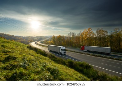 Trucks driving on the highway turning towards the horizon in an autumn landscape with sun shining through the clouds in the sky