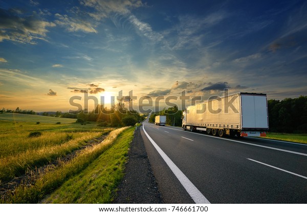 Trucks driving towards the setting sun on the\
road in rural\
countryside