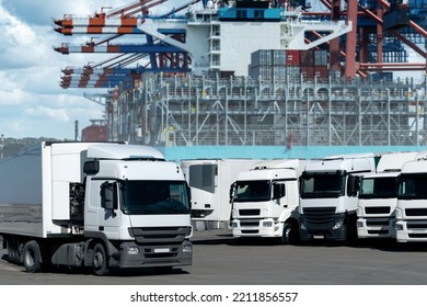 Trucks In The International Seaport Against On A Background Of A Ship Loaded With Containers. International Trade And Logistics Concept