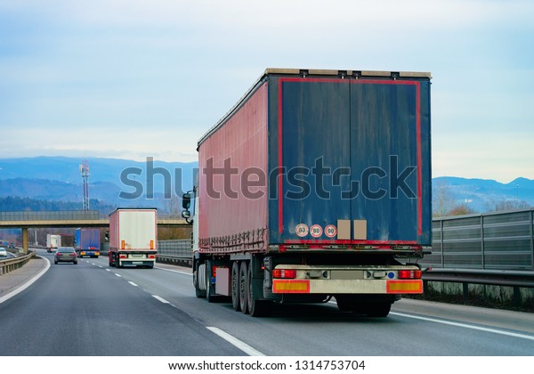 Trucks in road. Trucker in highway. Lorry doing\
logistics work. Semi trailer with driver. Big cargo car. Freight\
delivery. Transport export industry. Container with loaded goods on\
background. 