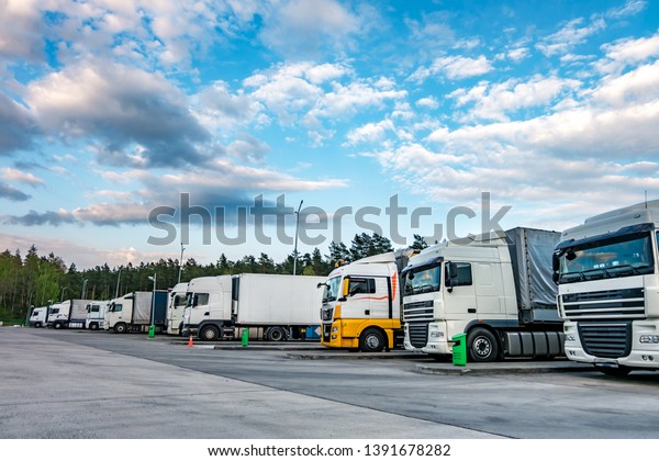 Trucks in a row with containers in\
the parking lot near forest , Logistic and Transport\
concept