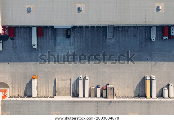 Trucks with\
trailers wait for the loading of goods for transportation in the\
loading warehouse. Aerial top view drone shot. A large transit\
cargo terminal with trucks and\
trailers.