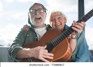 True happiness. Portrait of two sincere pensioners sitting together. Woman is cuddling man in cap while he is playing - Powered by Shutterstock