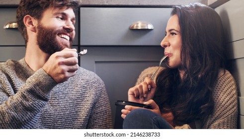 True Love Is When You Share Food. Shot Of A Happy Young Couple Sharing A Tub Of Ice Cream In Their Kitchen At Home.