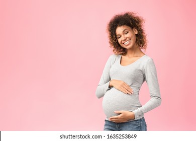 True mother love. African-american pregnant woman hugging her belly and smiling to camera, pink background with free space