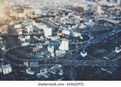 True tilt shift view from high point of highway overpass with multiple cars on evening in big city, shooting from top of road interchange with crosstown traffic on sunset in Bangkok, Thailand