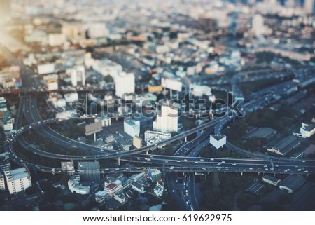 True tilt shift view from high point of highway overpass with multiple cars on evening in big city, shooting from top of road interchange with crosstown traffic on sunset in Bangkok, Thailand