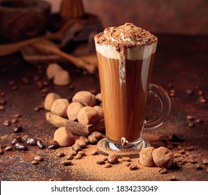 Truffles And Glass Of Hot Chocolate With Whipped Cream. Sweets And Drink Sprinkled With Cocoa Powder On An Old Brown Table.