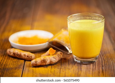 Trumeric orange golden milk with root and powder o a wooden table