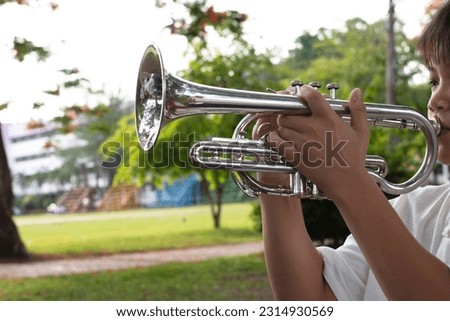 Trumpet instrument holding in hands of Asian student who is using fingers to press the top  vales of trumpet while learning it at school. Soft and selective focus on trumpet vales and fingers.
