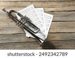 Trumpet and music sheets on wooden table, top view