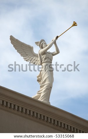 A trumpeting angel on top of a building against a blue sky.