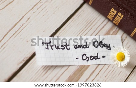 Trust and obey God and Jesus Christ always. Faith and hope in God's Word, Holy Bible for life. Living in obedience to God's commandments. Closed Bible with gold letters on wooden background.