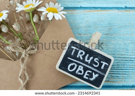 Trust and obey, handwritten words with flowers on vintage wood table. Top view. Faith, obedience, belief in God Jesus Christ. Inspiring Christian message. Biblical concept.