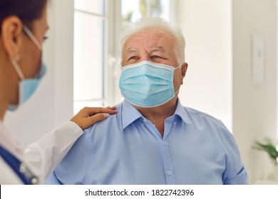 Trust And Support. Happy Senior Patient And Doctor, Wearing Medical Face Masks, Communicating In Hospital Office. General Practitioner In Modern Clinic Patting Aged Man On The Shoulder Cheering Him Up