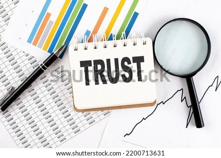TRUST text on a notebook on the graph background with pen and magnifier