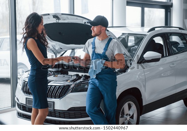 I trust you. Woman in the\
auto salon with employee in blue uniform taking her repaired car\
back.