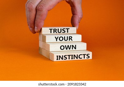 Trust your own instincts symbol. Wooden blocks with words 'Trust your own instincts'. Beautiful orange background. Businessman hand. Copy space. Business and trust your own instincts concept.