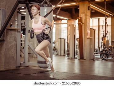TRX Training. Young athletic redhead woman in sports clothing training with trx fitness straps in the gym.