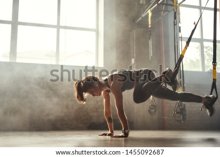 TRX Training. Young athletic woman in sports clothing training legs with trx fitness straps in the gym.