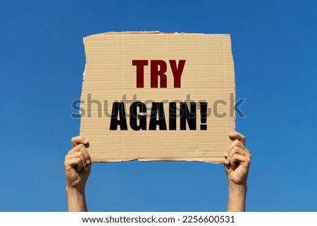 Try again message on box paper held by 2 hands with blue sky background. This note can be used for business concept about encouraging people to try again.