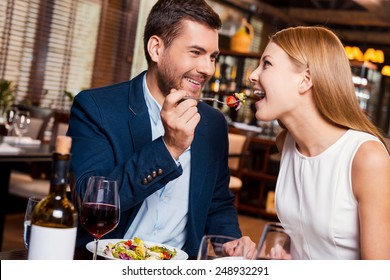 Try this! Beautiful young loving couple enjoying dinner at the restaurant while man feeding his girlfriend with salad