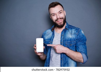 Try this device. Handsome young smiling guy in denim shirt showing a finger on the phone with a white screen. - Shutterstock ID 782975932