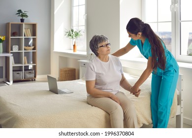 Trying to make patient's life happier. Female home care nurse supports and assists senior woman with all her daily needs. Caregiver holds old lady's hand, helps her stand up from bed and talks to her