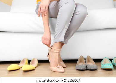 Trying on shoes by elegant lady sitting on white sofa background