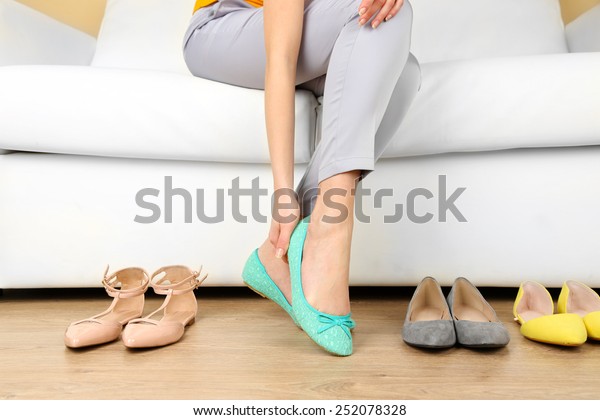 Trying on shoes by elegant lady sitting on\
white sofa background