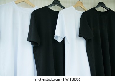 T-shirts are black and white, on a hanger, on a light background. Fashionable, modern, youth clothes. Clothing made from natural materials, cotton. T-shirts on a light background without inscriptions.