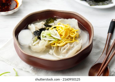 Tteok Mandu Guk, Korean Dumpling and Rice Cake Soup. Close Up, on White Marble Table. 