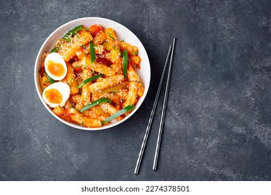 Tteokbokki with eggs, fresh green leek and  roasted sesame seeds in  bowl on thу dark  table, top view. Tteok-bokki is a   Korean cuisine dish with rice gnocchi sticks and spacy sauce.  Asian food