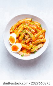 Tteokbokki with eggs, fresh green leek and roasted sesame seeds on the white table top. Tteok-bokki is a Korean cuisine dish with rice gnocchi sticks and spacy sauce. Asian food, fast Korean food