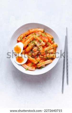 Tteokbokki with eggs, fresh green leek and  roasted sesame seeds in blue  bowl on the white  table top. Tteok-bokki is a   Korean cuisine dish with rice gnocchi sticks and spacy sauce.  Asian food