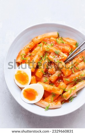 Tteokbokki with eggs, fresh green leek and roasted sesame seeds on the white table top. Tteok-bokki is a Korean cuisine dish with rice gnocchi sticks and spacy sauce. Asian food, fast Korean food
