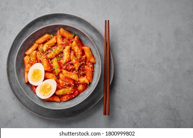 Tteokbokki with eggs in gray bowl on concrete table top. Tteok-bokki is a korean cuisine dish with rice cakes. Asian food. Top view. Copy space