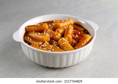 Tteokbokki with white sesame in white bowl with grey background. Tteok-bokki is a korean cuisine dish with rice cakes. Asian food. 