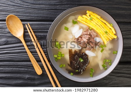 Tteokguk or sliced rice cake soup is a traditional Korean dish eaten during the celebration of the Korean New Year closeup in the bowl on the table. Horizontal top view from above